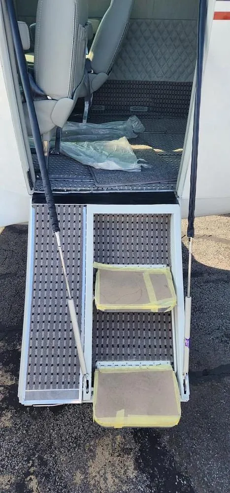 The open entry door and retractable steps of an aircraft, with protective cardboard on the steps and a view into the cabin.