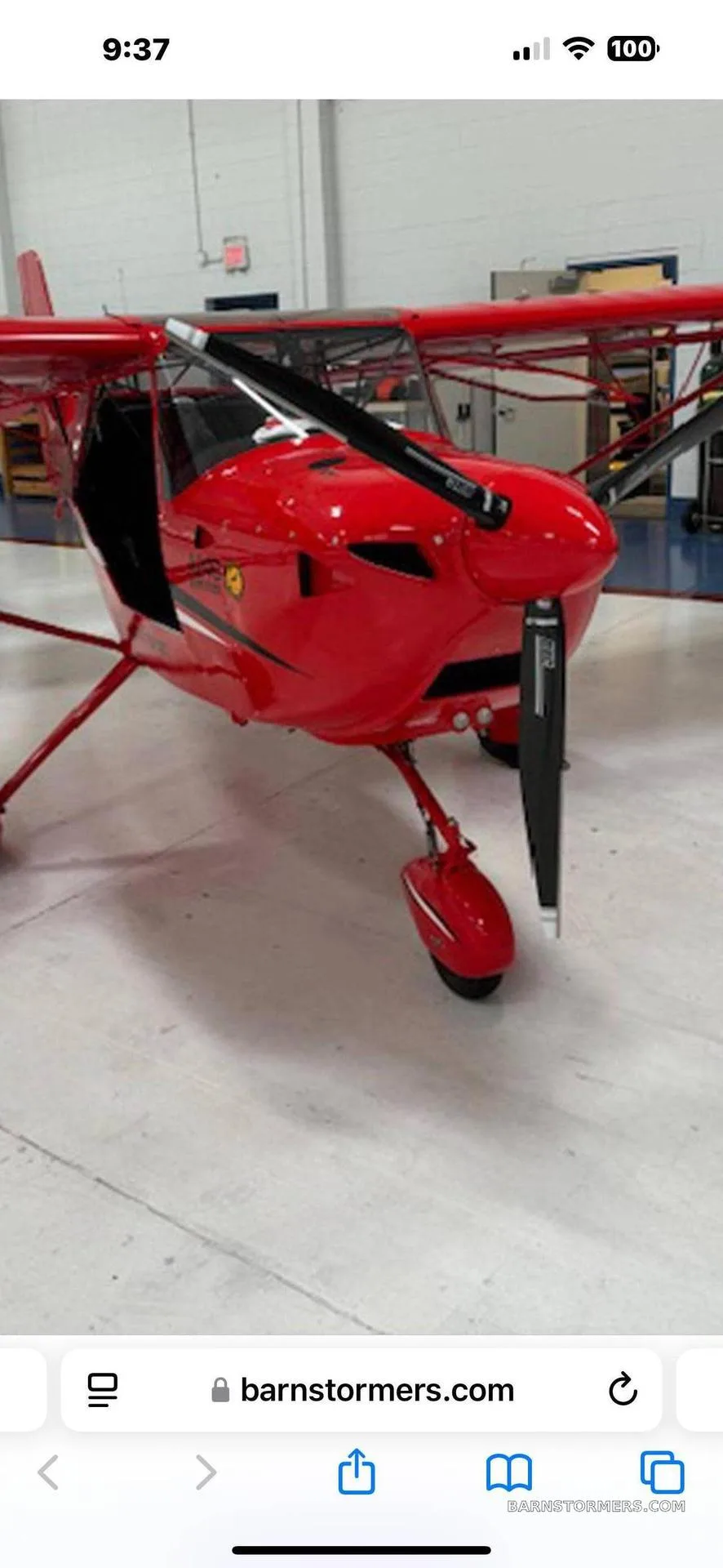 A red Aerotrek A240 light-sport aircraft with a black propeller, parked inside a hangar.