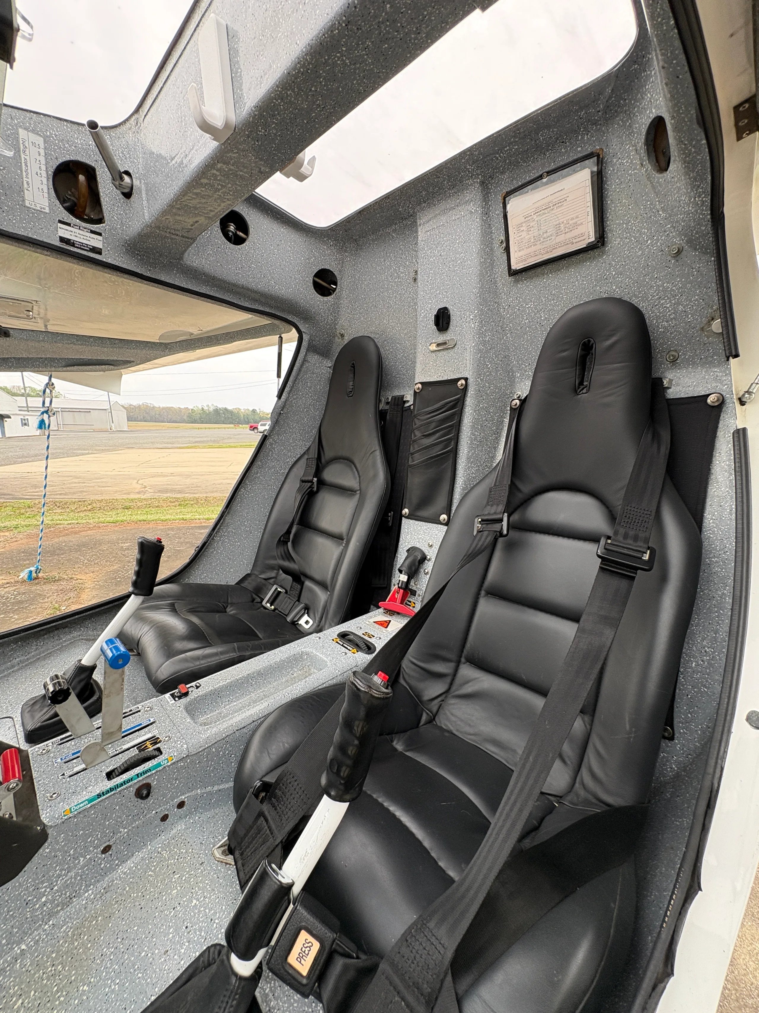 The interior of the aircraft shows two black leather seats and flight controls in a grey speckled cabin.