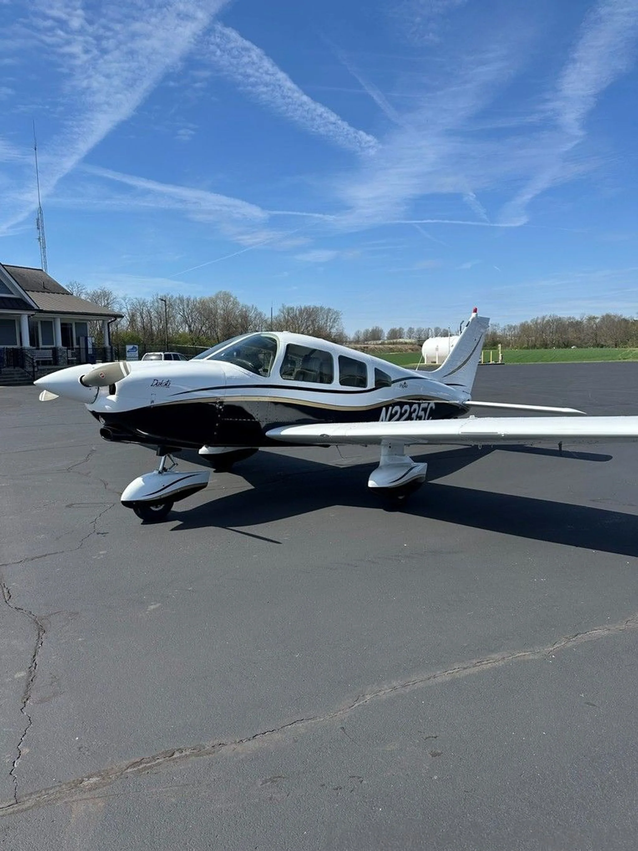 A white and black Piper aircraft with gold trim, registration N2235C, parked on an asphalt ramp.