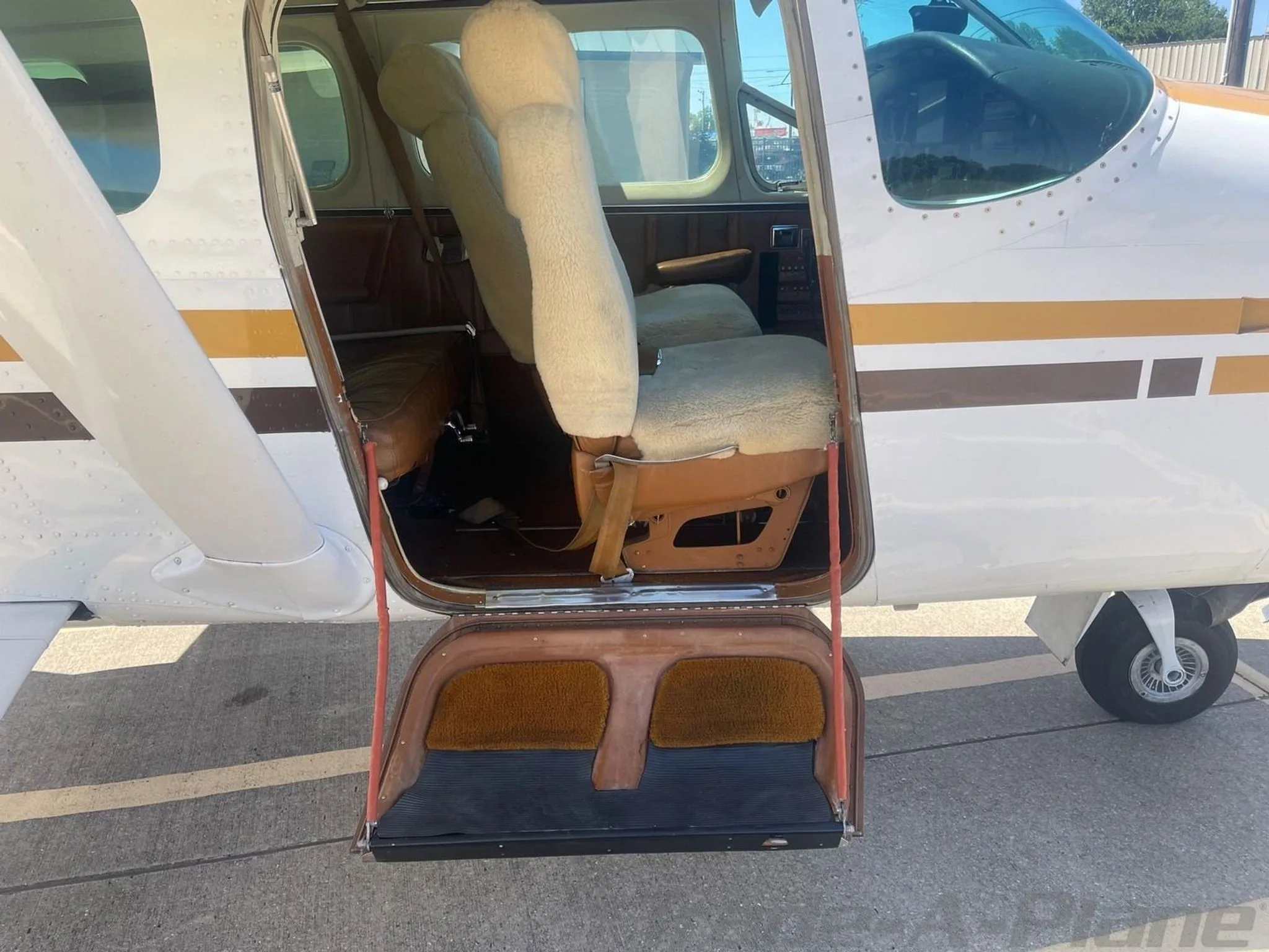The open cargo door and step of a Cessna 206, revealing the interior seats with sheepskin covers.