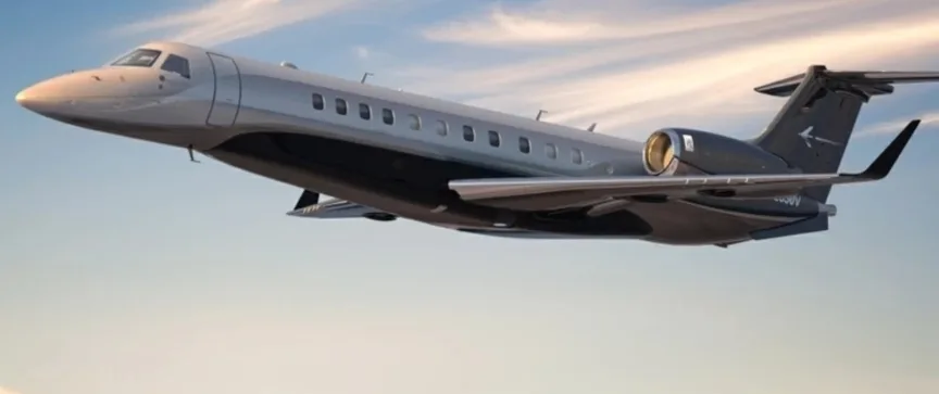 A sleek silver and dark grey business jet is shown in flight against a partly cloudy sky.