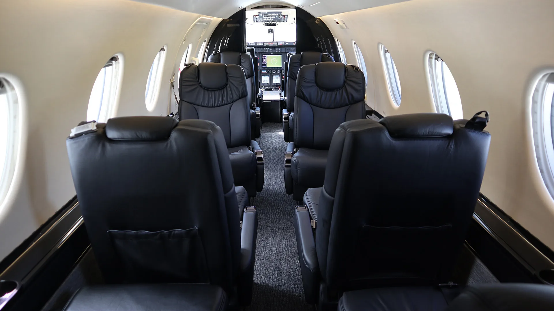The interior cabin of a private jet with black leather seats, looking forward towards the cockpit.
