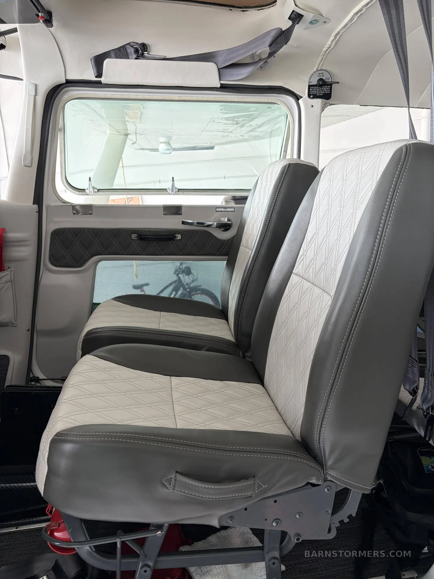 The aircraft's interior cabin, showing two rows of gray and white quilted seats with a view out the window.