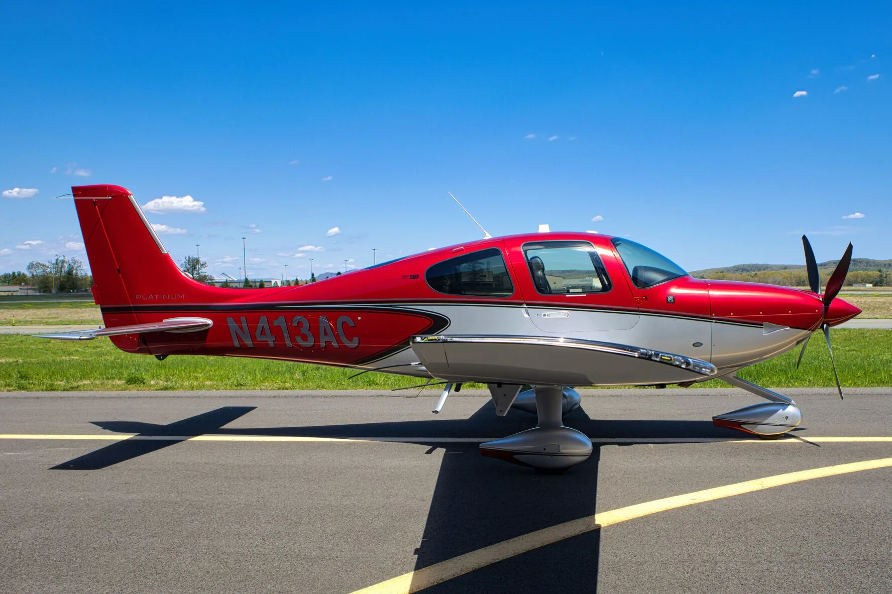 A red and silver Cirrus SR22T aircraft, N413AC, parked on an airport tarmac under a clear blue sky.