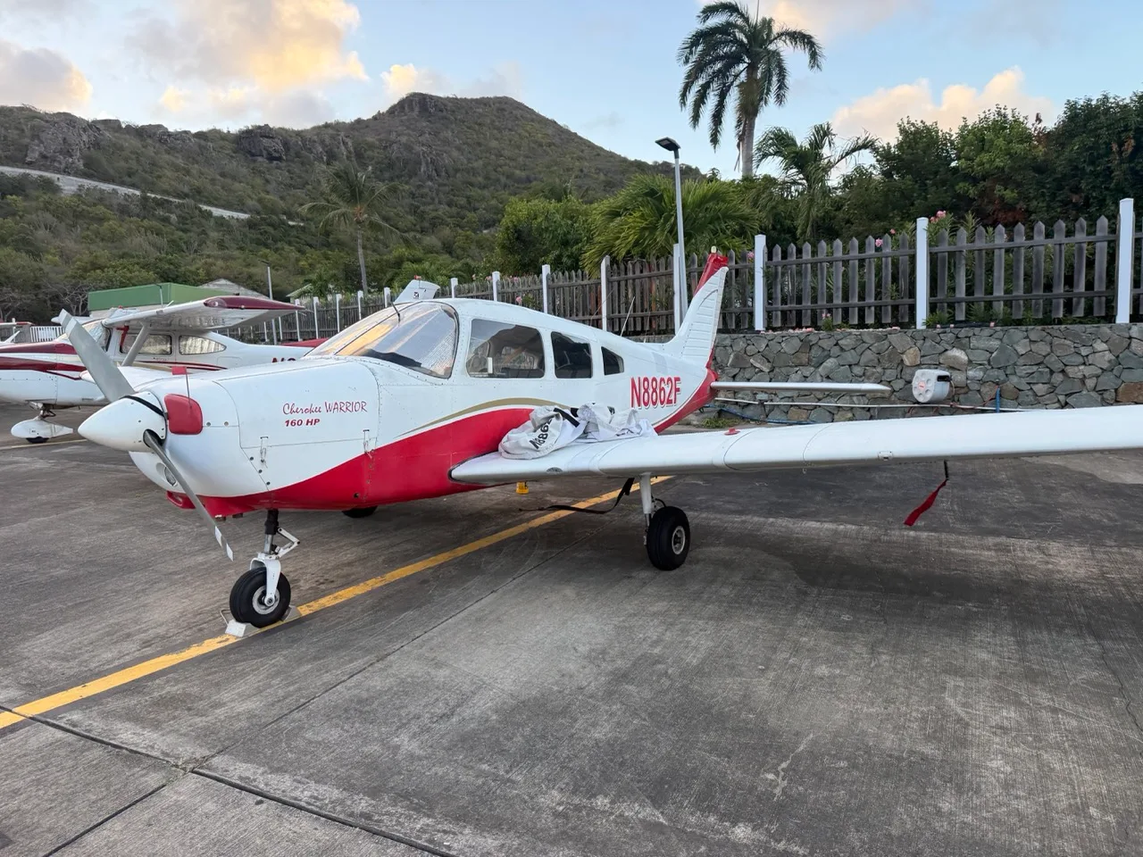 A white and red Piper Cherokee Warrior 160 HP aircraft (N8862F) parked on an airfield with mountains in the background.