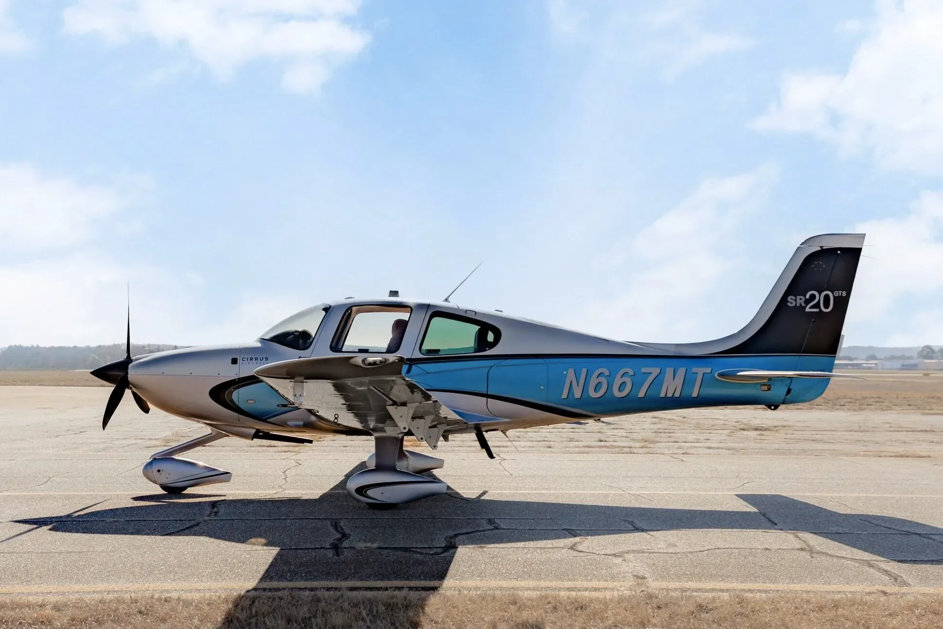 A Cirrus SR20 GTS aircraft with N667MT registration, featuring a silver and blue paint scheme, parked on an airfield.
