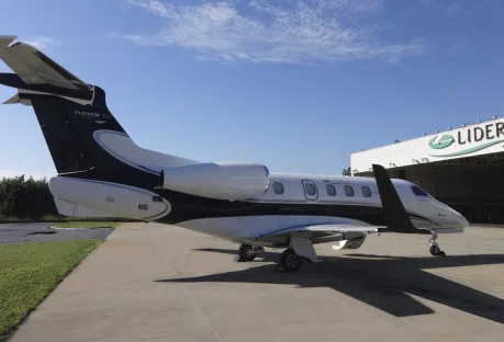 A Phenom 300E aircraft with a black and white paint scheme is parked on the tarmac.