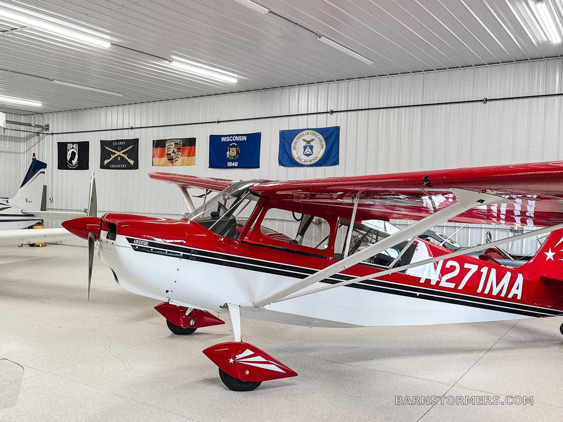 A red and white single-engine aircraft with tail number N271MA is parked inside a brightly lit hangar.