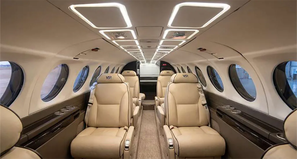 The interior cabin of a private aircraft with light beige leather seats and overhead lighting.