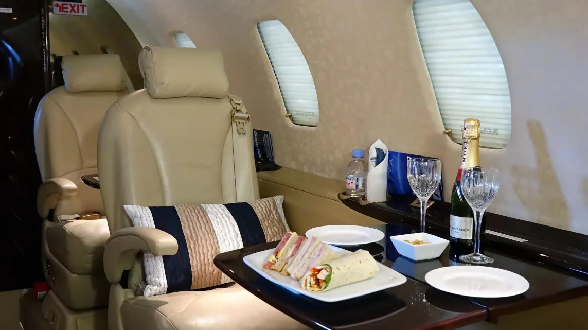 Close-up of aircraft interior with leather seats, a table set with food and drinks.