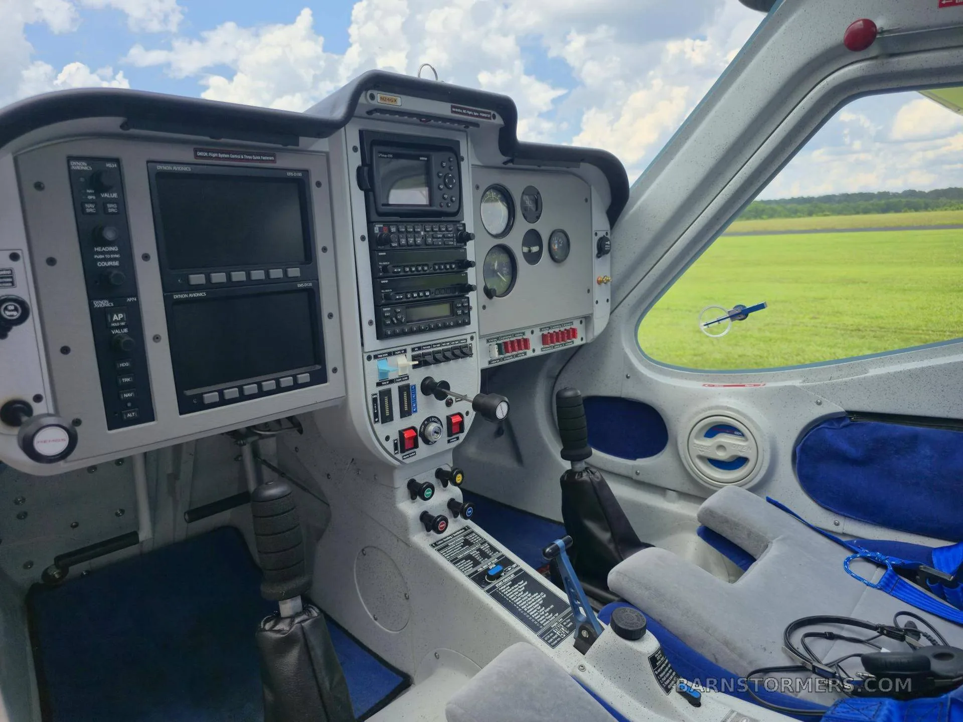 The cockpit of a light sport aircraft features a grey instrument panel with multiple screens and controls, and blue seats.