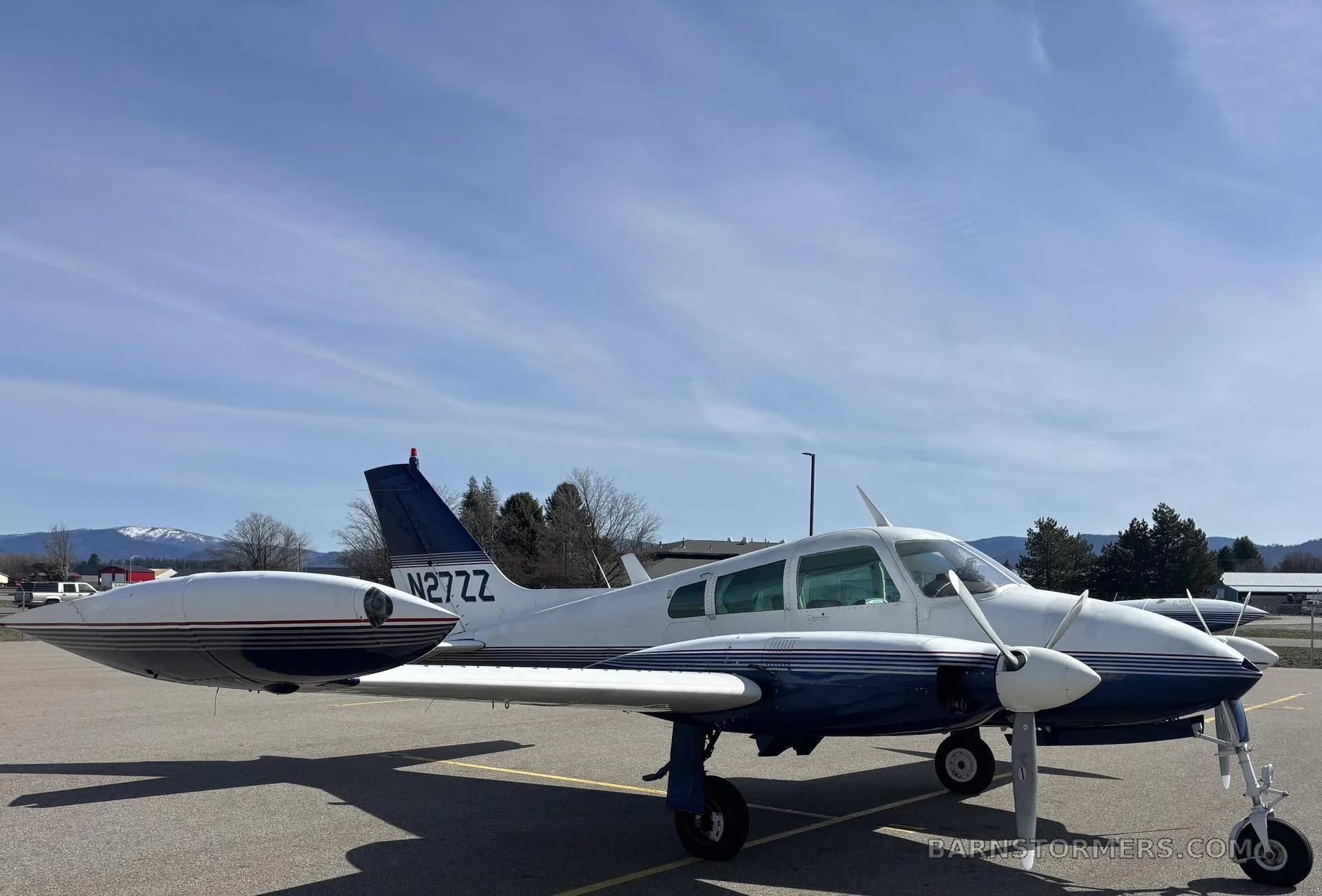 A white and blue Cessna 310I, registration N27ZZ, parked on an airfield with mountains in the background.