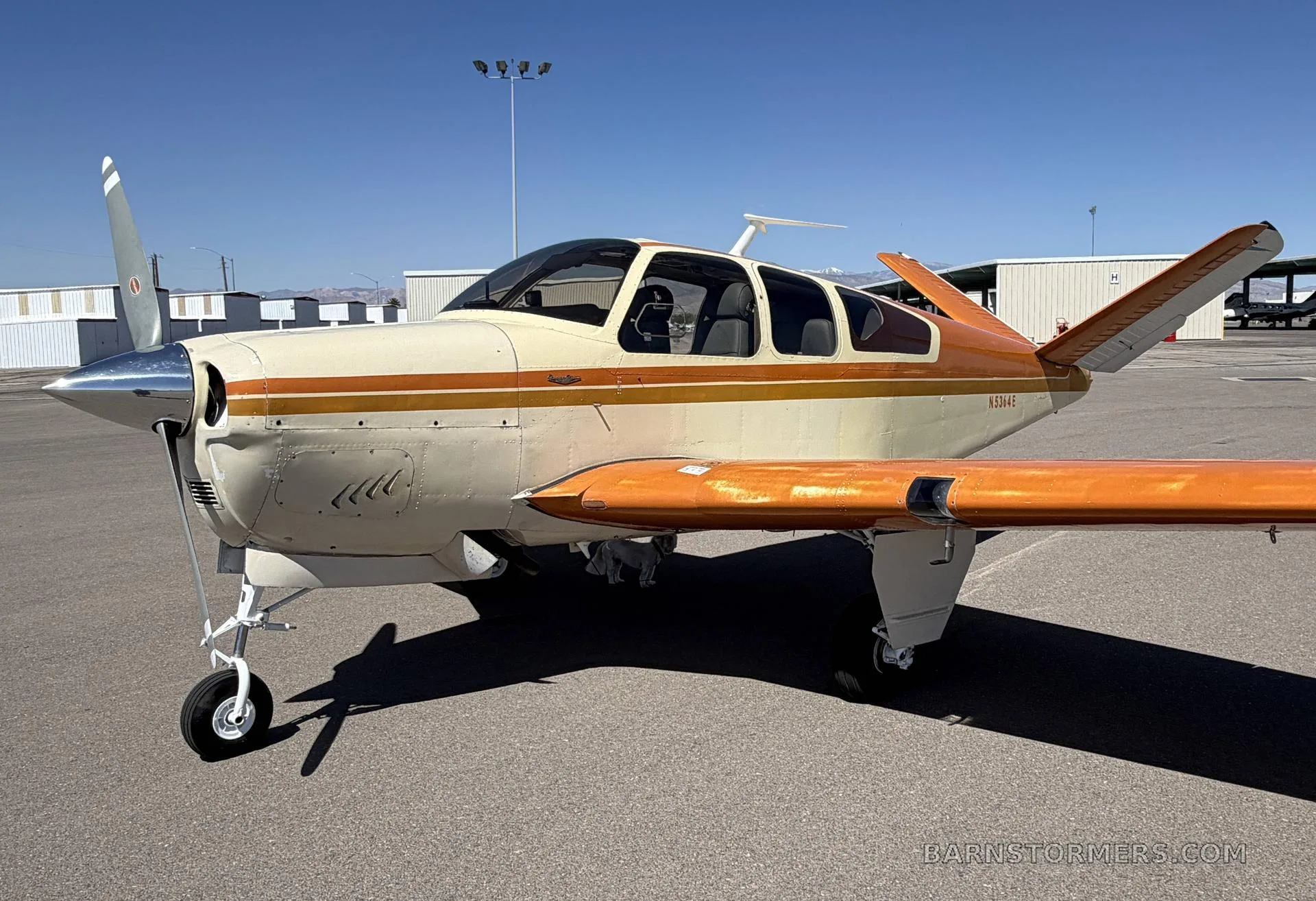 A cream and orange single-engine aircraft with tail number N5364E parked on an airfield, viewed from the front-left.