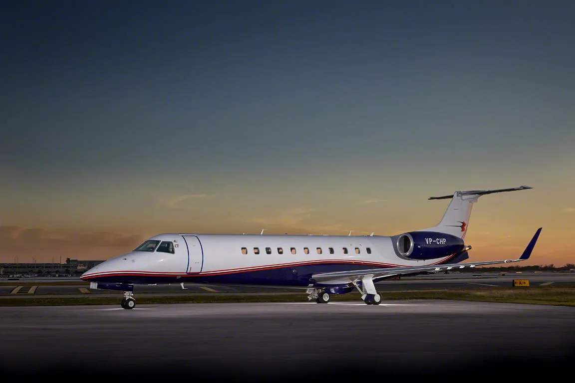 A side view of the VP-CHP Embraer Legacy 650 business jet with white and blue livery on an airfield at sunset.