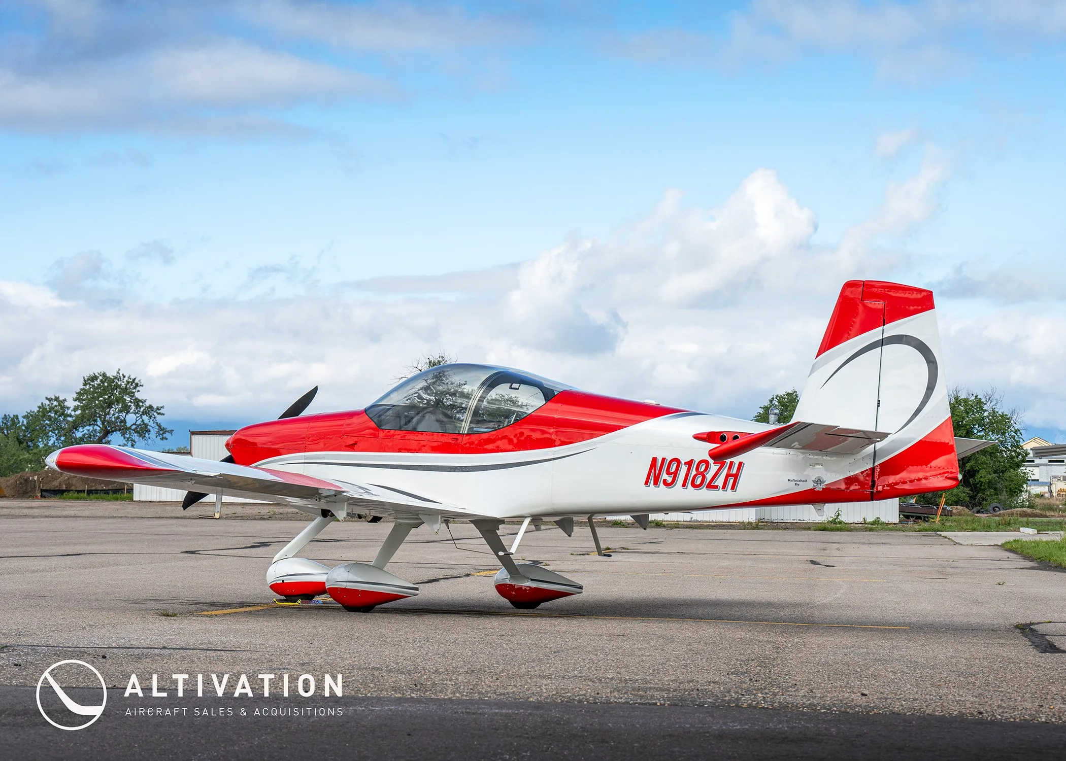 A side view of the red and white N918ZH aircraft with a distinctive tail design, parked on an airfield.