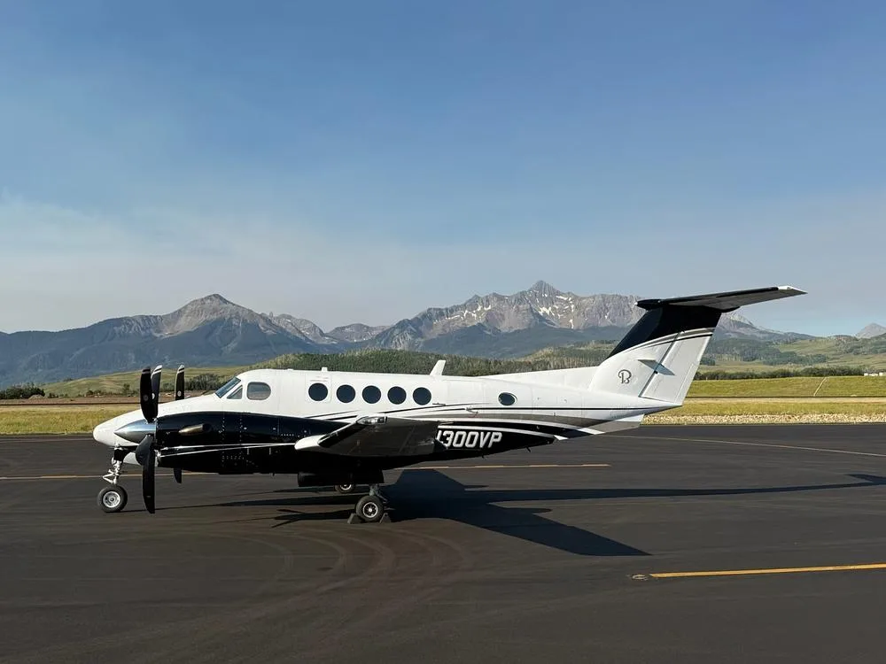 A black and white Beechcraft King Air 350, registration N300VP, is parked on an airfield with mountains in the background.