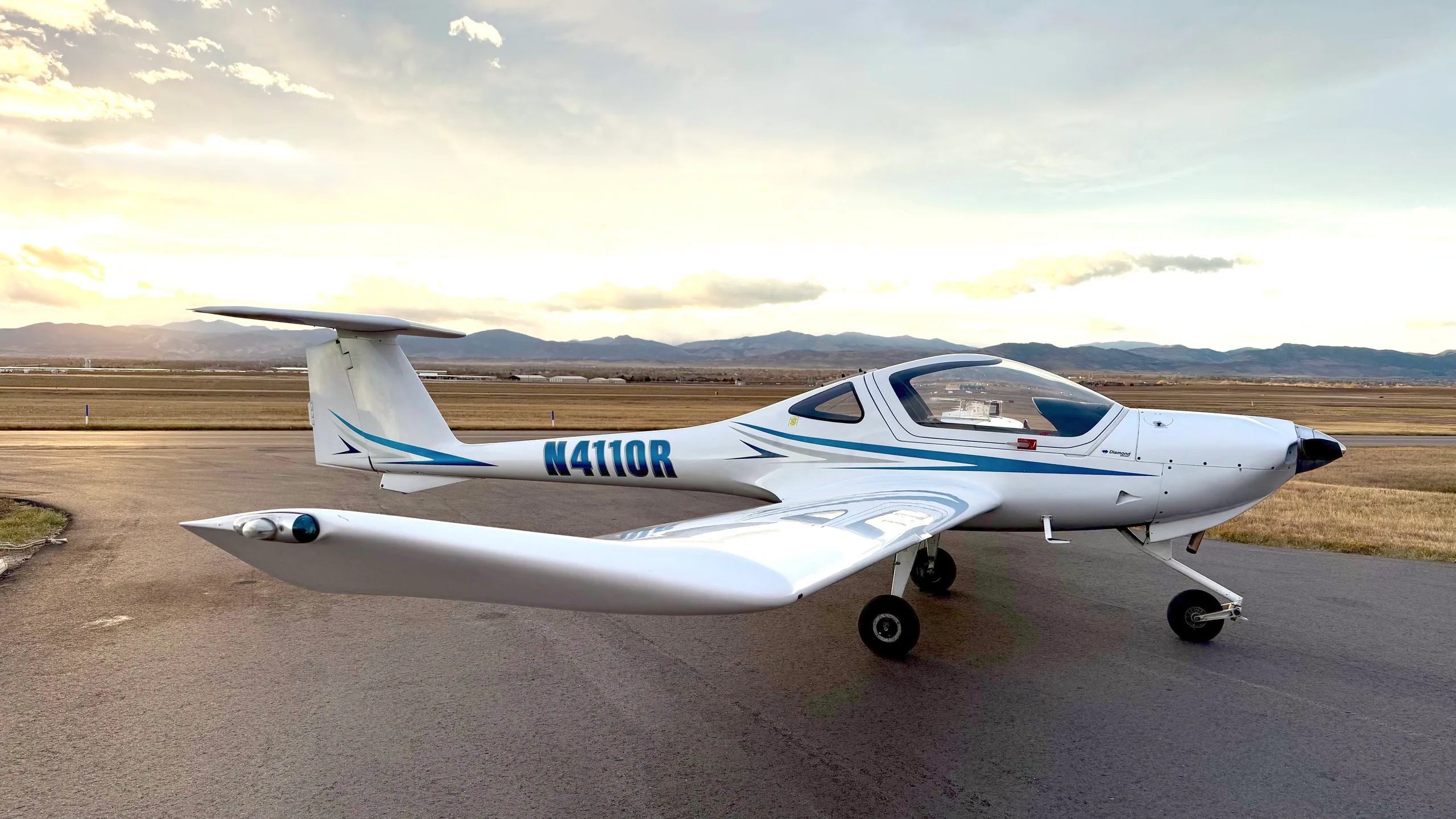 A white Diamond DA20-C1 Eclipse aircraft with blue stripes, registration N4110R, parked on an airfield at sunset.