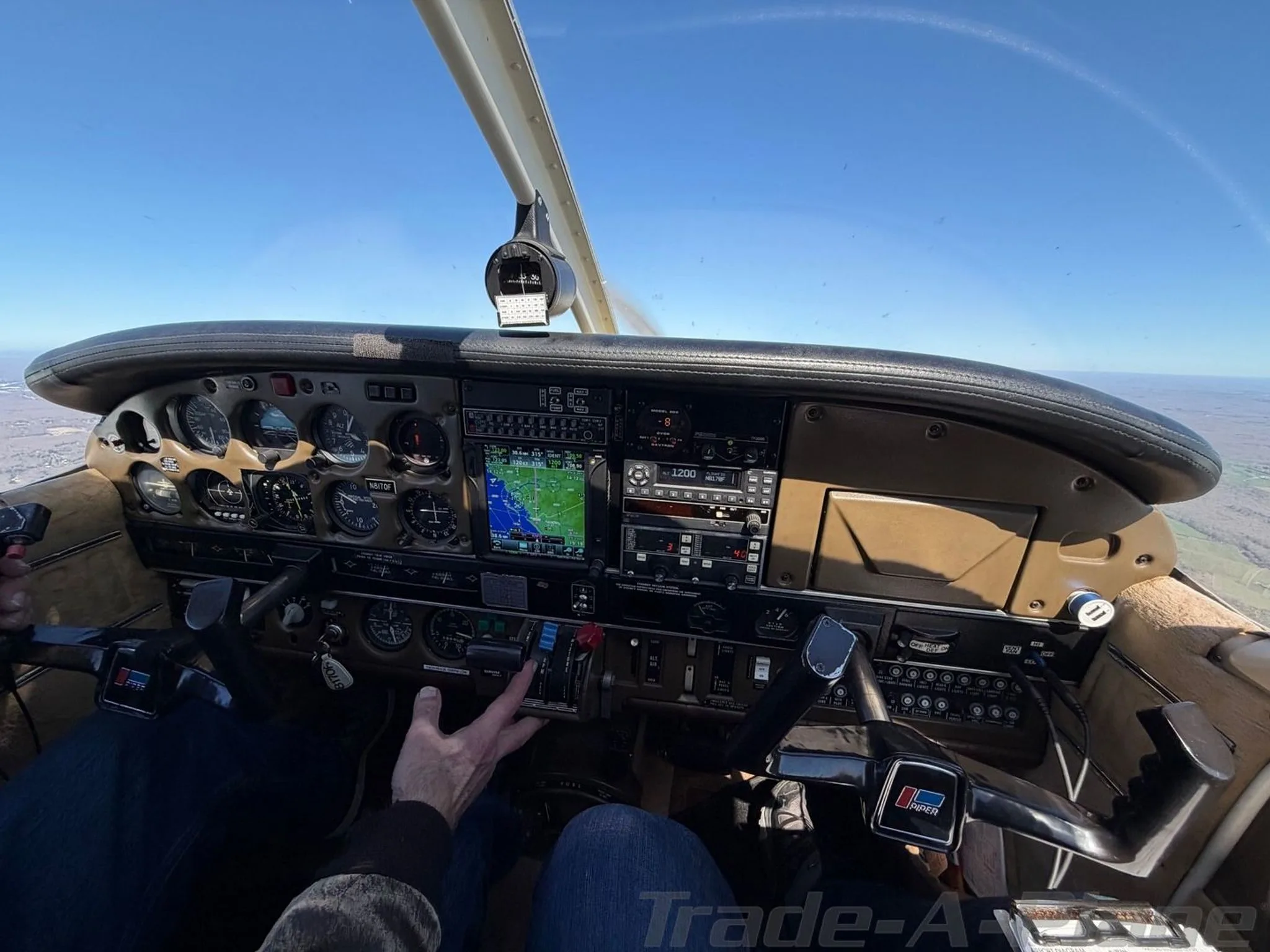 The cockpit of a Piper Cherokee aircraft in flight, showing the instrument panel, controls, and a pilot's hands.
