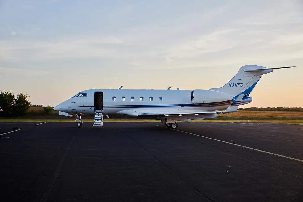 A white Bombardier Challenger 300 private jet with blue stripes, registration N311FC, and an open entry door on an airfield.