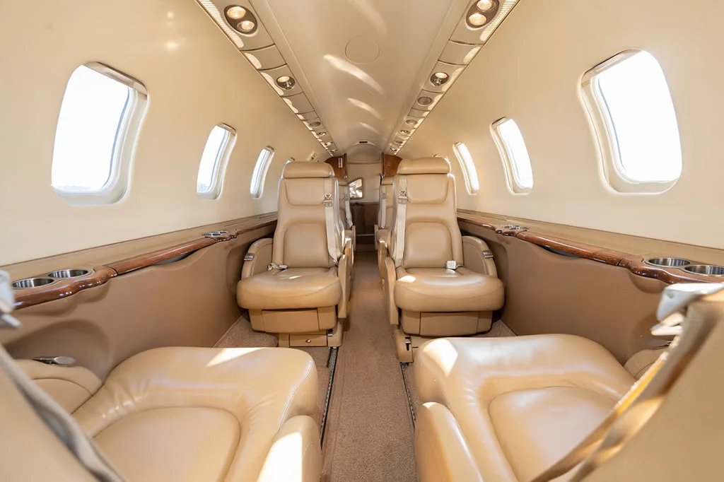 View down the aircraft cabin aisle with beige leather seats on both sides.
