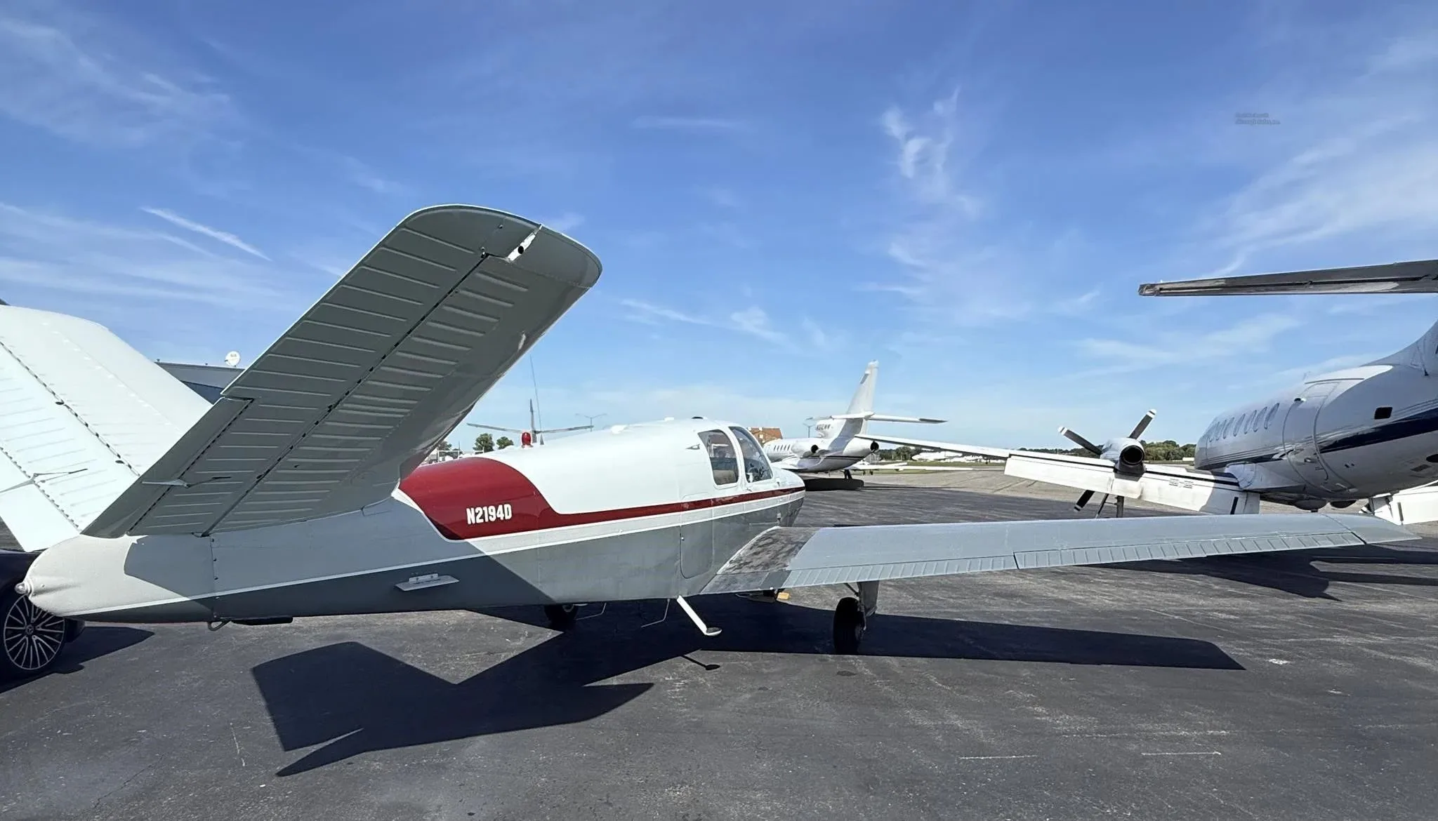 Rear-side view of the N2194D Beechcraft Bonanza V-tail aircraft, showing its white and grey paint scheme with a red stripe.