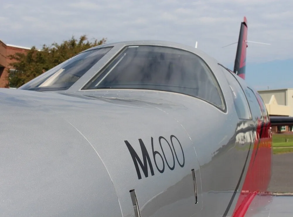 A close-up view of the cockpit windows and silver fuselage of a Piper M600 aircraft.