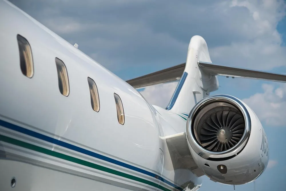 A close-up view of the rear fuselage, engine, and tail of a white Bombardier Challenger 300 jet with blue and green stripes.