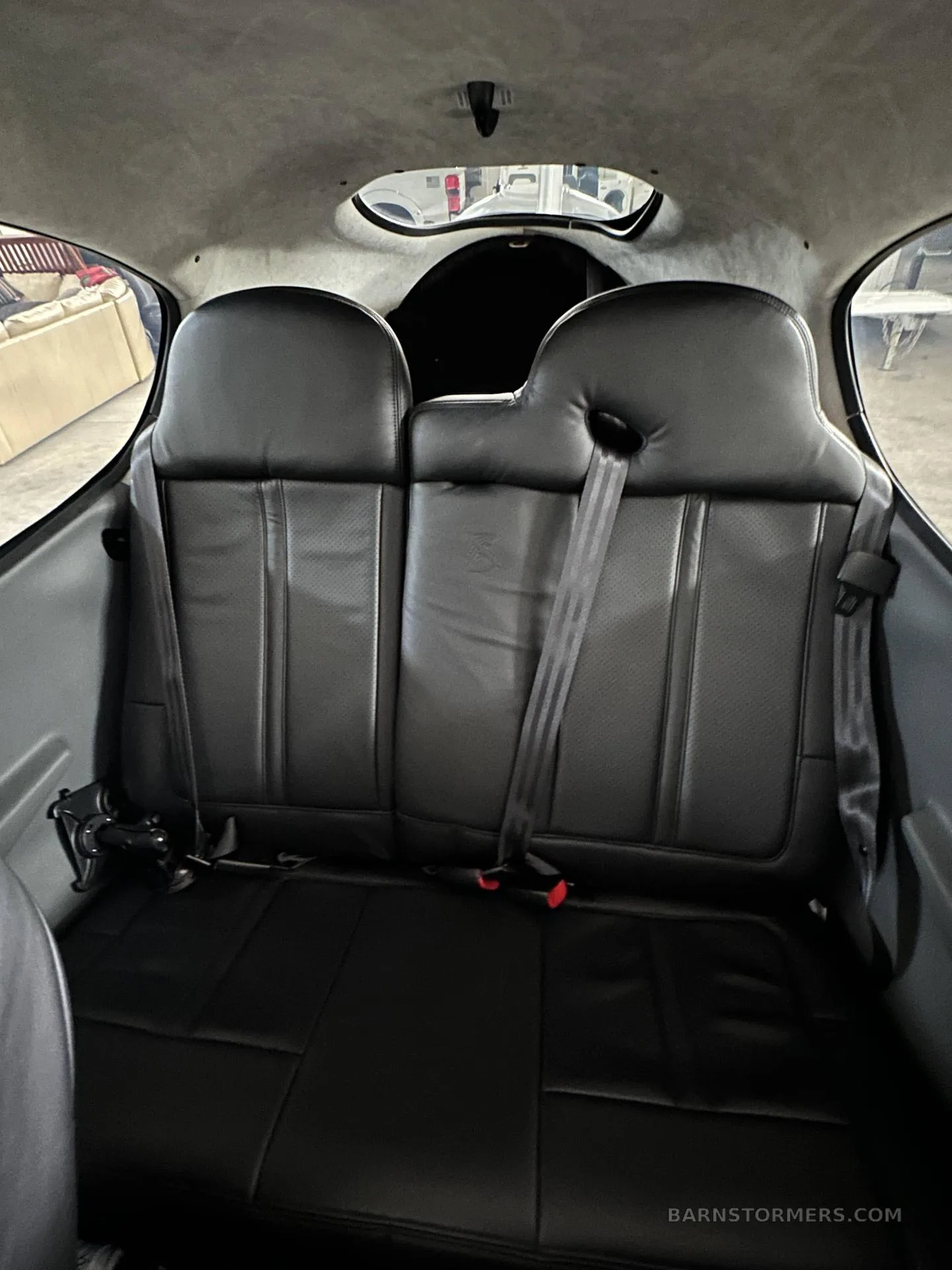 The rear black leather seats of a small aircraft cabin, with seatbelts and a small window above.