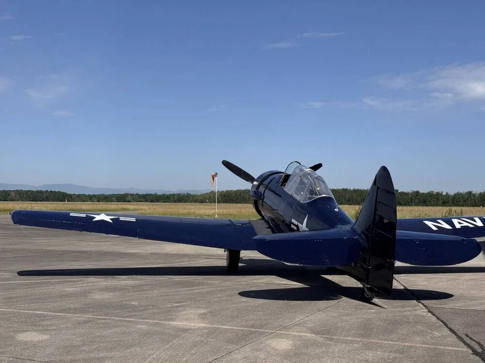 A dark blue North American T-6 Texan aircraft with "NAVY" on its wing is parked on an airfield under a clear blue sky.