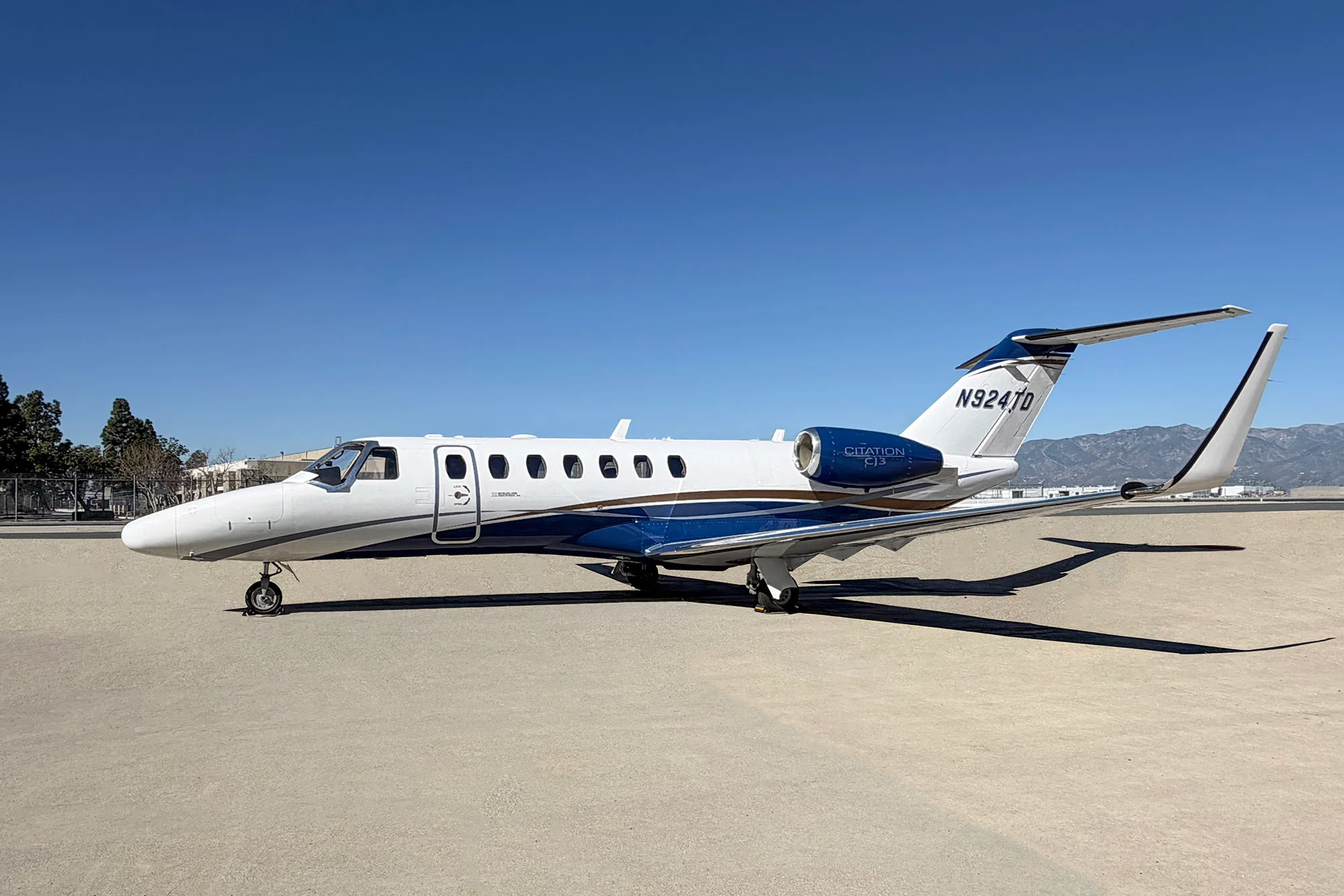 A white and blue Cessna Citation CJ3 private jet with registration N924TD is parked on a tarmac under a clear blue sky.