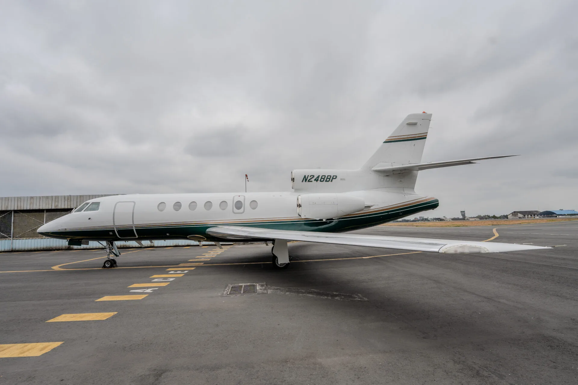 A side view of a white and green private jet (N248BP) parked on an airfield under a cloudy sky.
