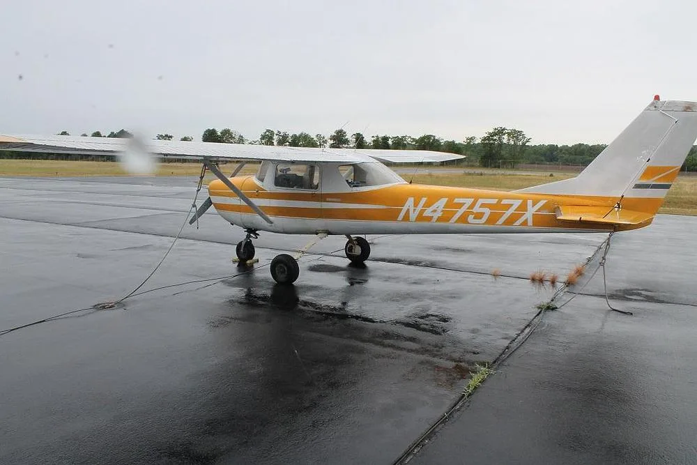 A rear-side view of a yellow and white Cessna 150 (or similar) with registration N4757X parked on a wet tarmac.