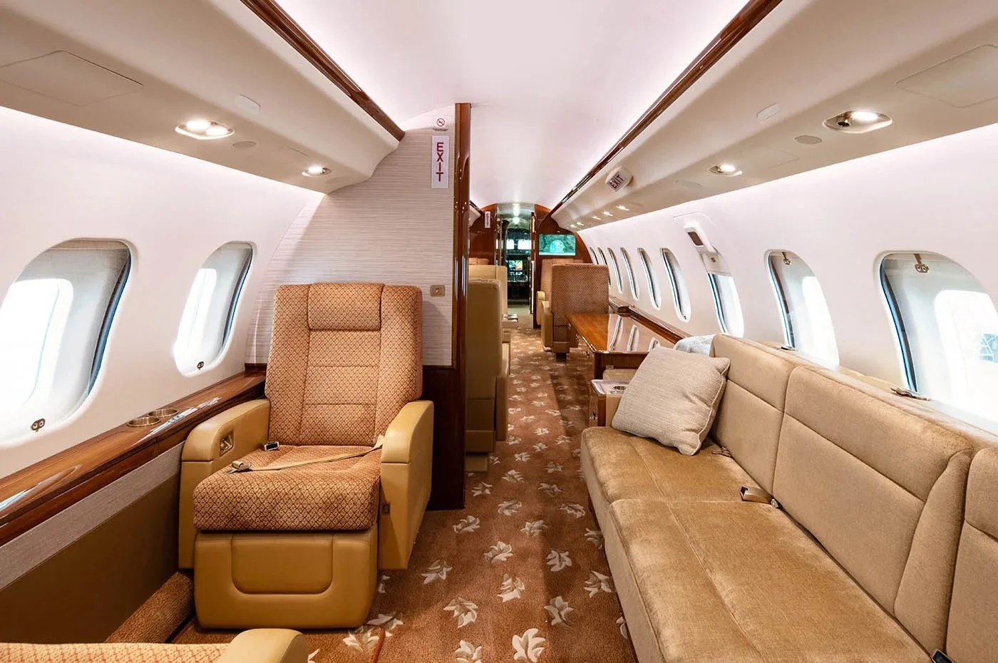 A view inside the aircraft cabin shows a beige sofa, a single seat, and an "EXIT" sign above the aisle.