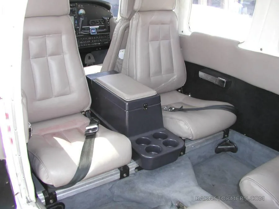 The aircraft's interior cabin with light gray leather seats, a center console with cup holders, and a partial view of the cockpit.