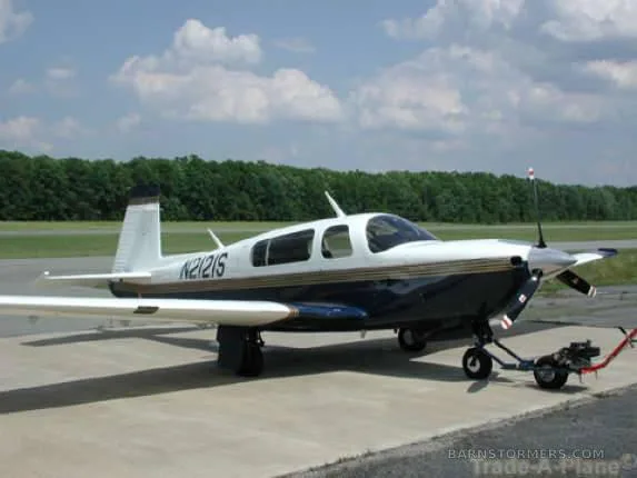 A white and blue single-engine propeller aircraft (N2121S) is parked on an asphalt ramp with a tow bar attached, under a partly cloudy sky.
