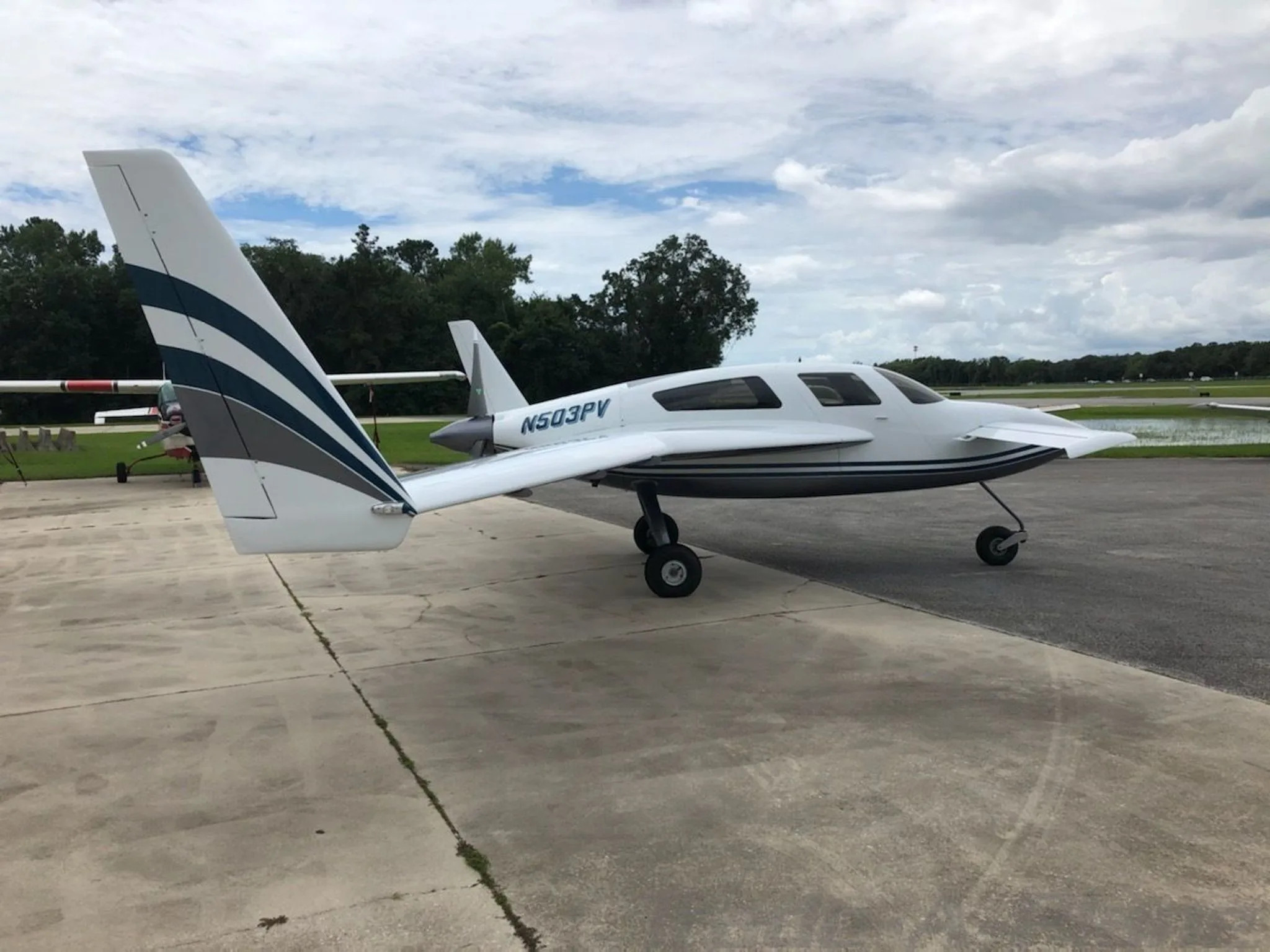 Side view of a white and dark grey Velocity aircraft with N503PV registration parked on an airfield under a cloudy sky.
