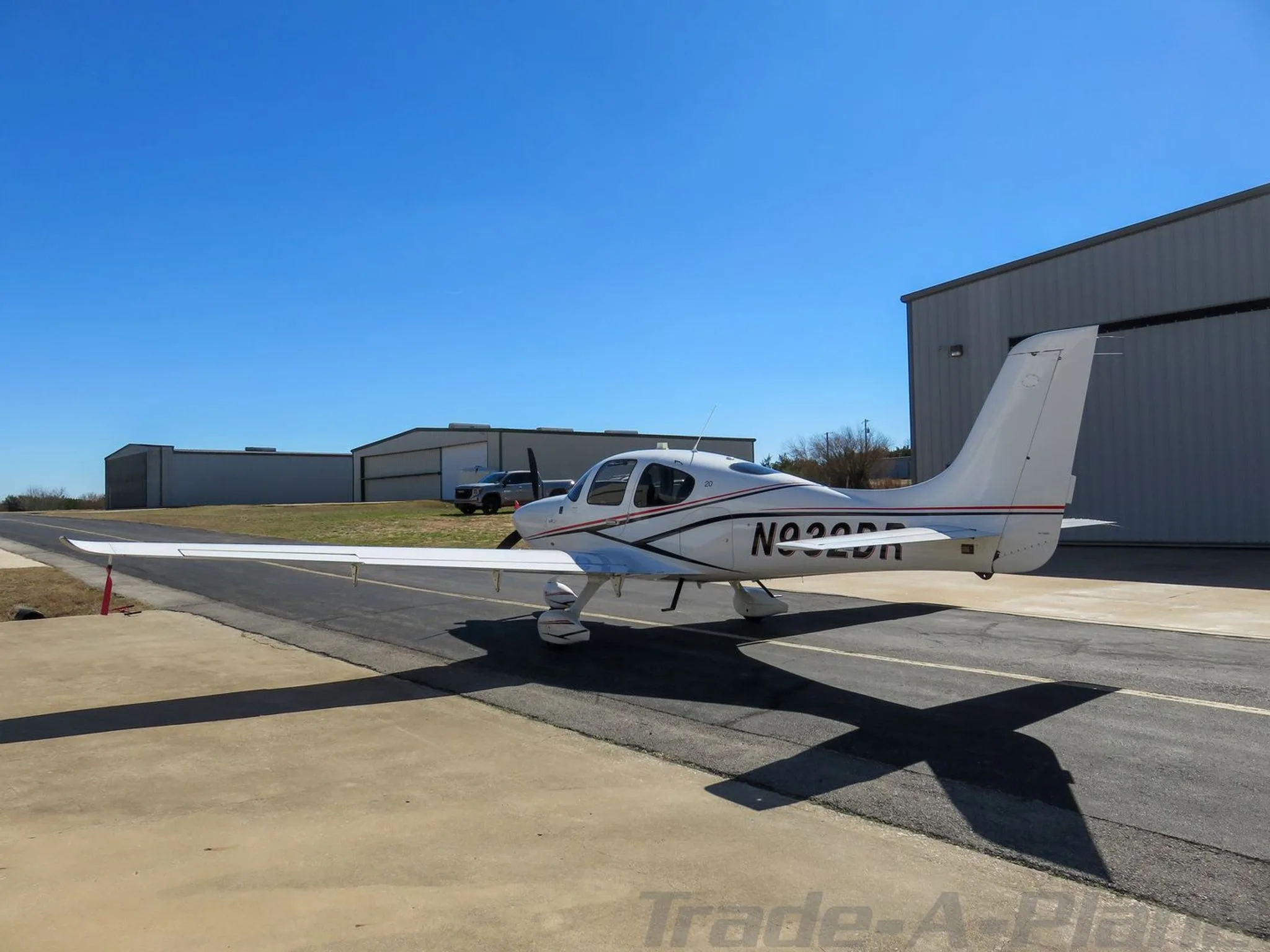 Three-quarter rear view of a white single-engine aircraft with red and black stripes, registration N932DR, parked on a tarmac.