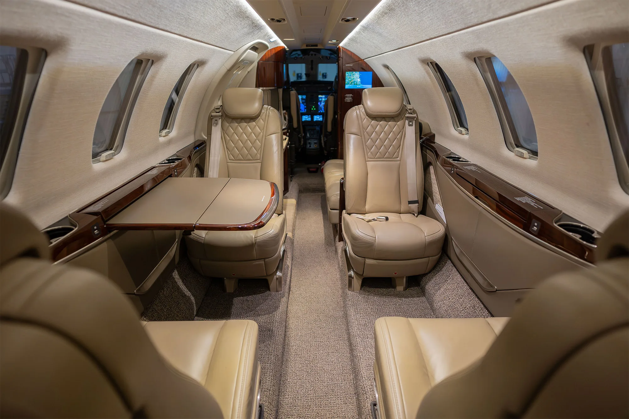 The interior cabin of a business jet with beige leather seats and a deployed side table, looking towards the cockpit.