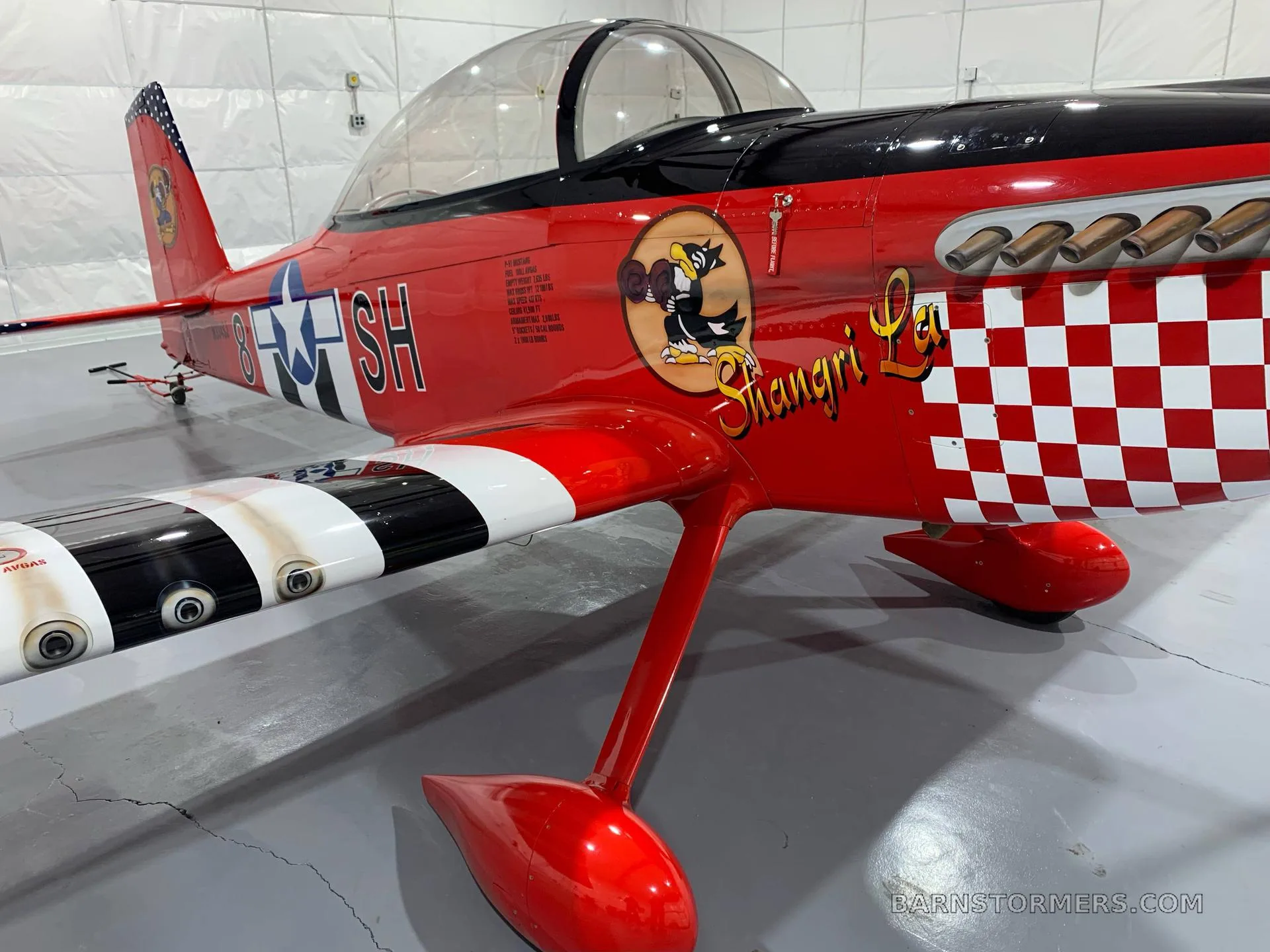 A close-up view of the red aircraft's fuselage showing a cartoon character and "Shangri La" text, with a checkered nose.