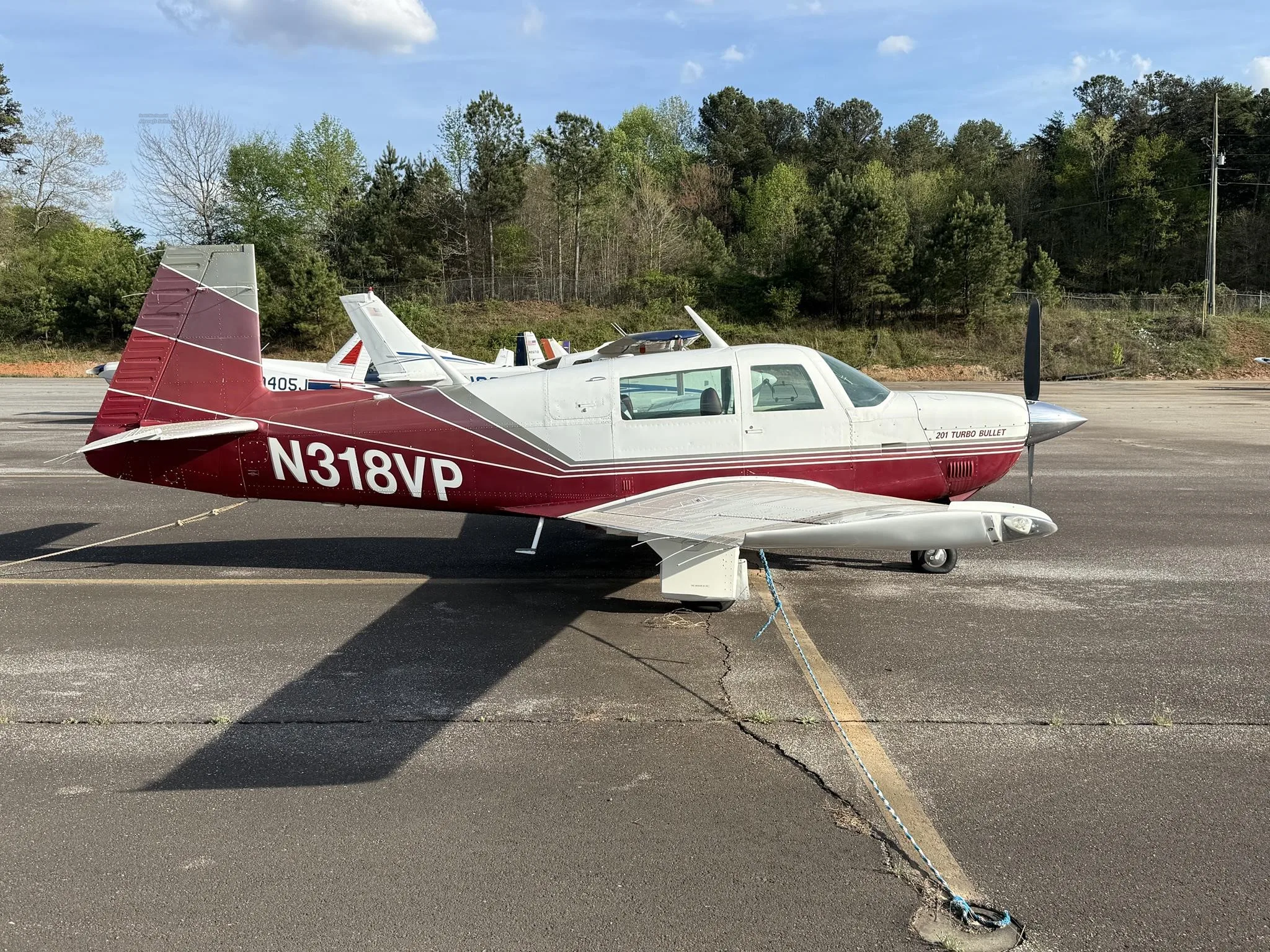 A red and white Mooney 201 Turbo Bullet aircraft, N318VP, parked on an asphalt ramp with trees in the background.