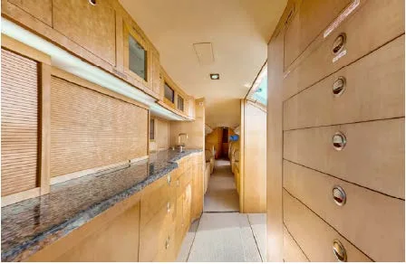 A view down the aircraft cabin from the galley, showing light wood cabinetry and a narrow aisle leading to passenger seating.