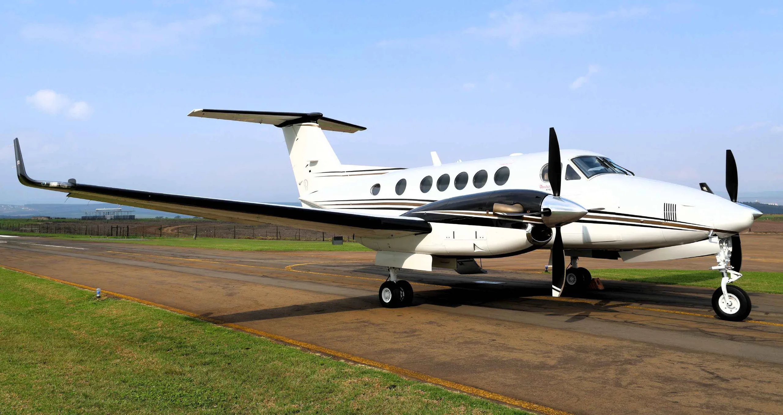 A white and black Beechcraft King Air 250 turboprop aircraft parked on an asphalt runway with green grass on the side.