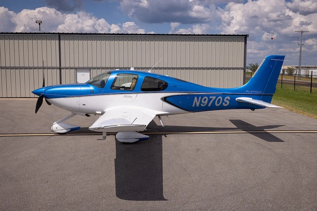 A side view of the blue and white Cirrus SR22 aircraft, N970S, parked on an asphalt ramp next to a hangar.