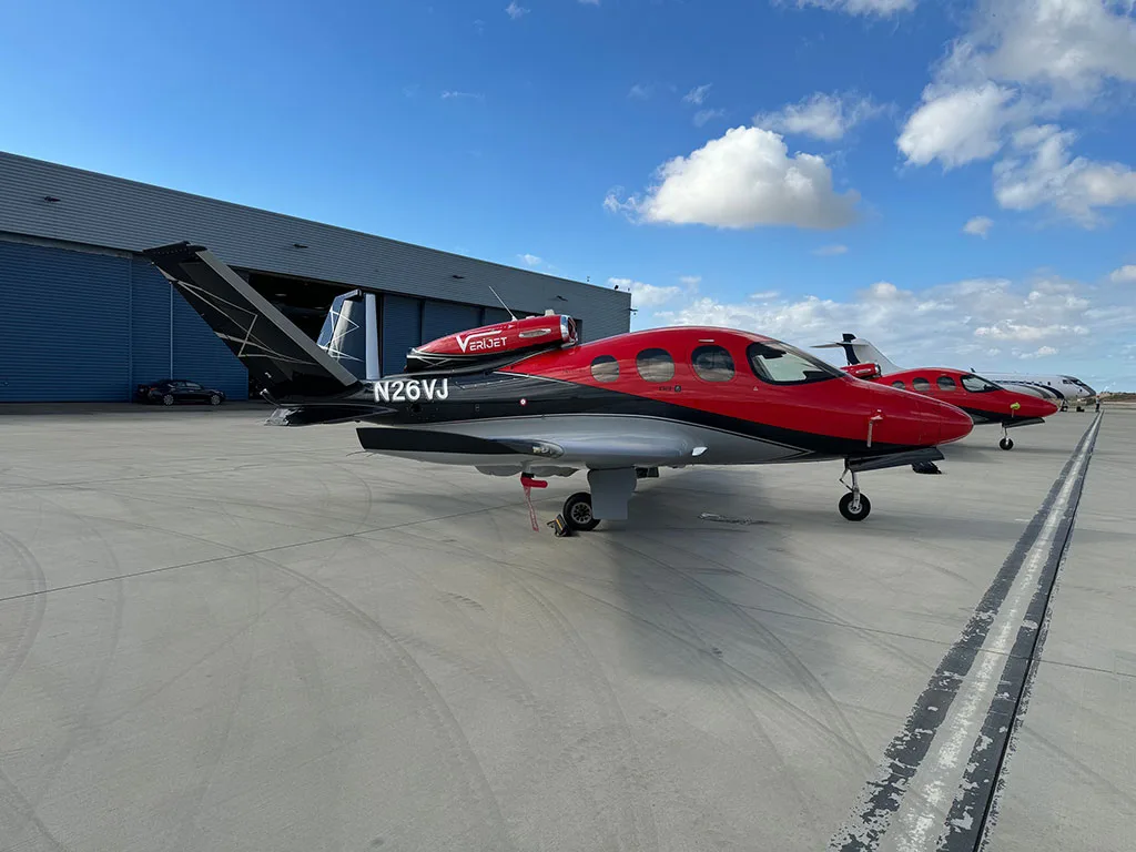 A red, black, and silver Cirrus Vision Jet (N26VJ) parked on an airport tarmac with a hangar in the background.