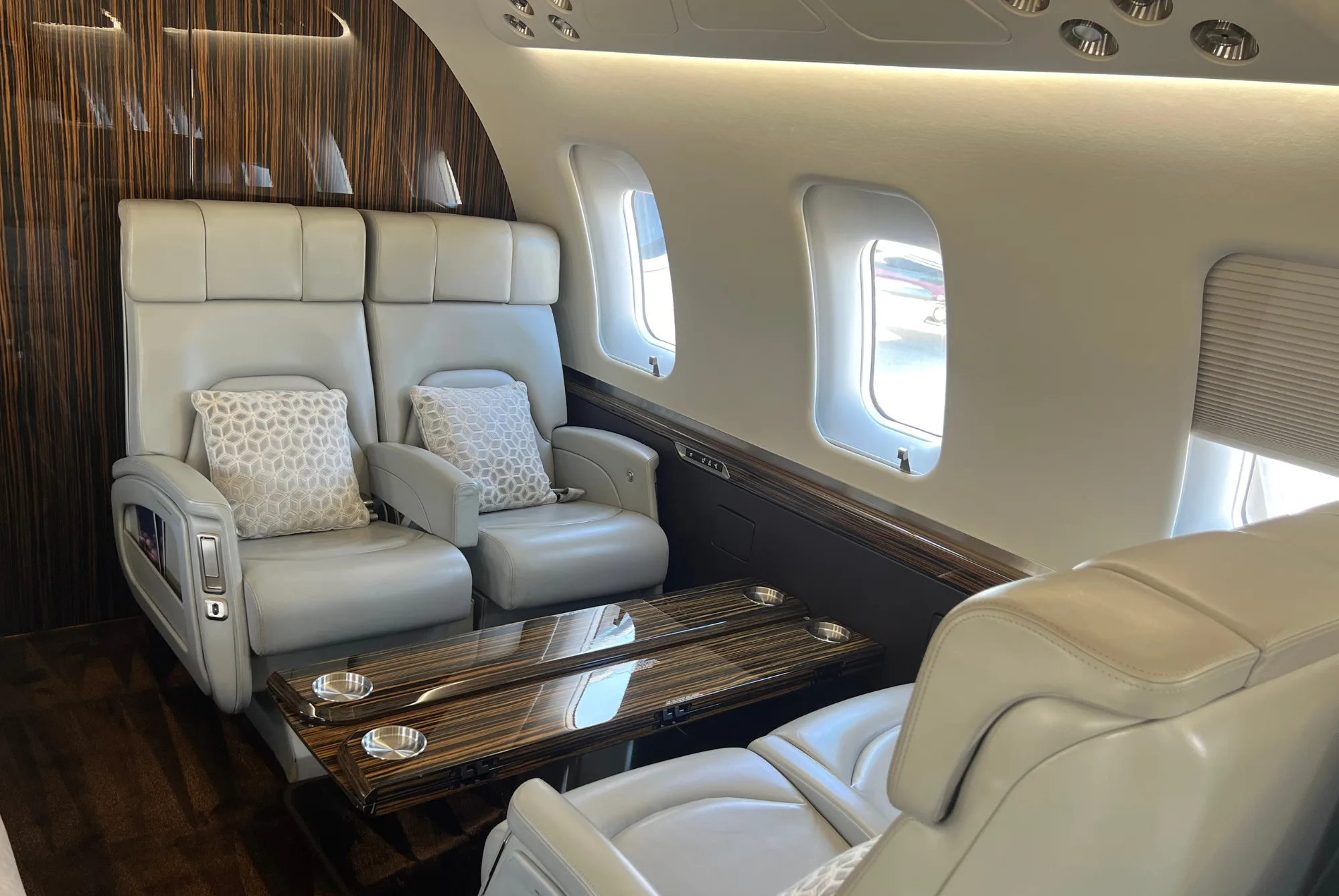 Two light grey leather seats and a wooden table in an aircraft cabin.
