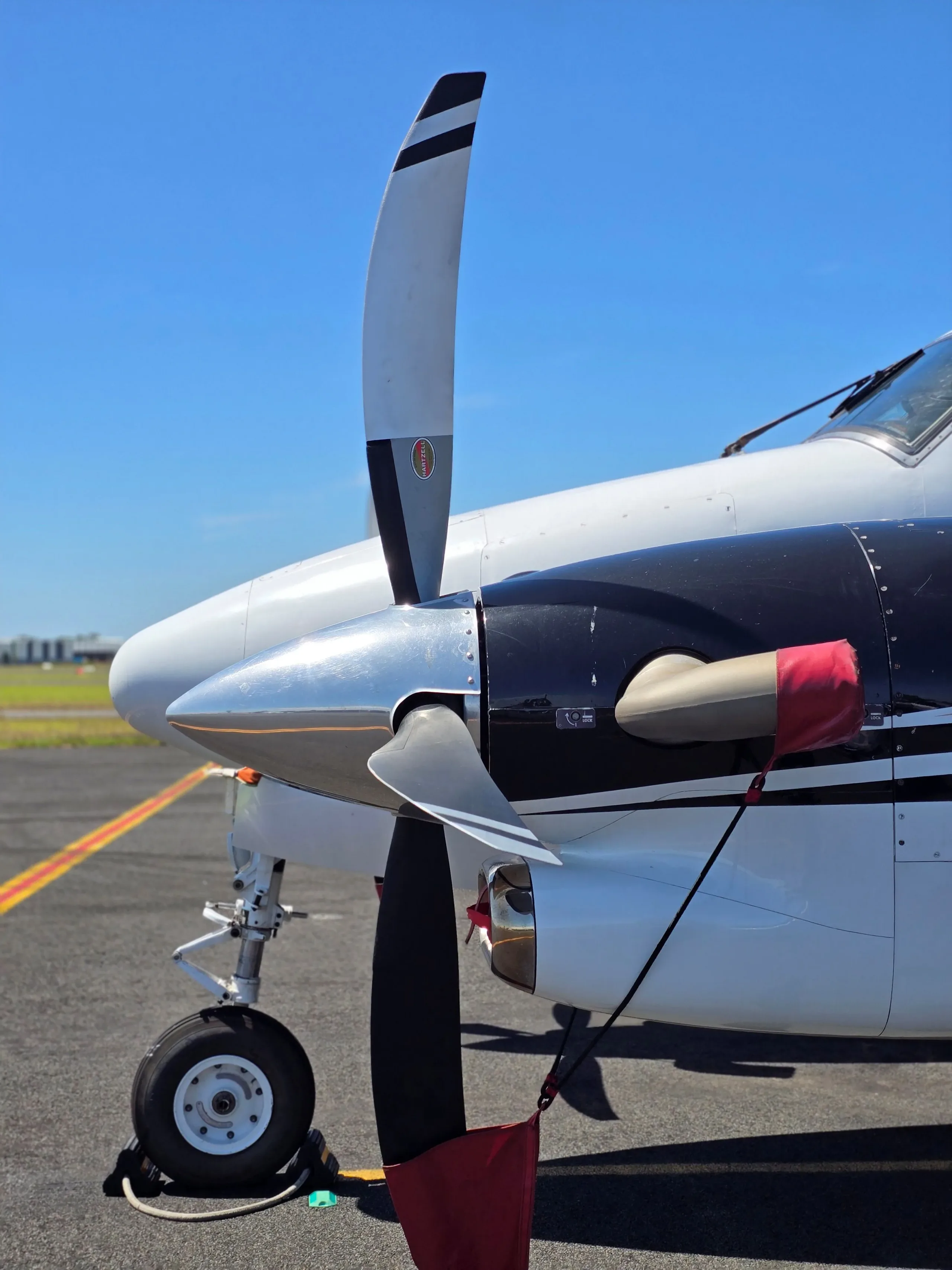 A close-up view of the propeller and nose of a white and black Beechcraft King Air on a tarmac.