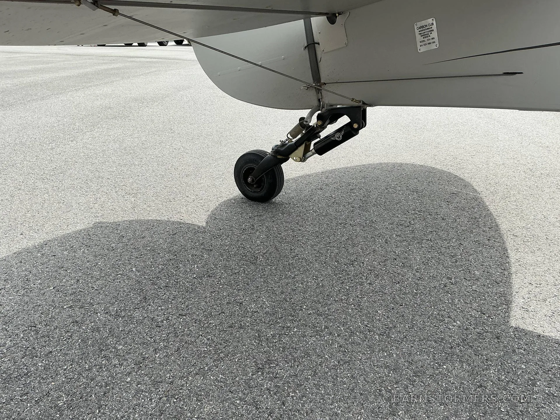 A close-up view of the small tailwheel and its strut assembly under the rear fuselage of a light grey aircraft.