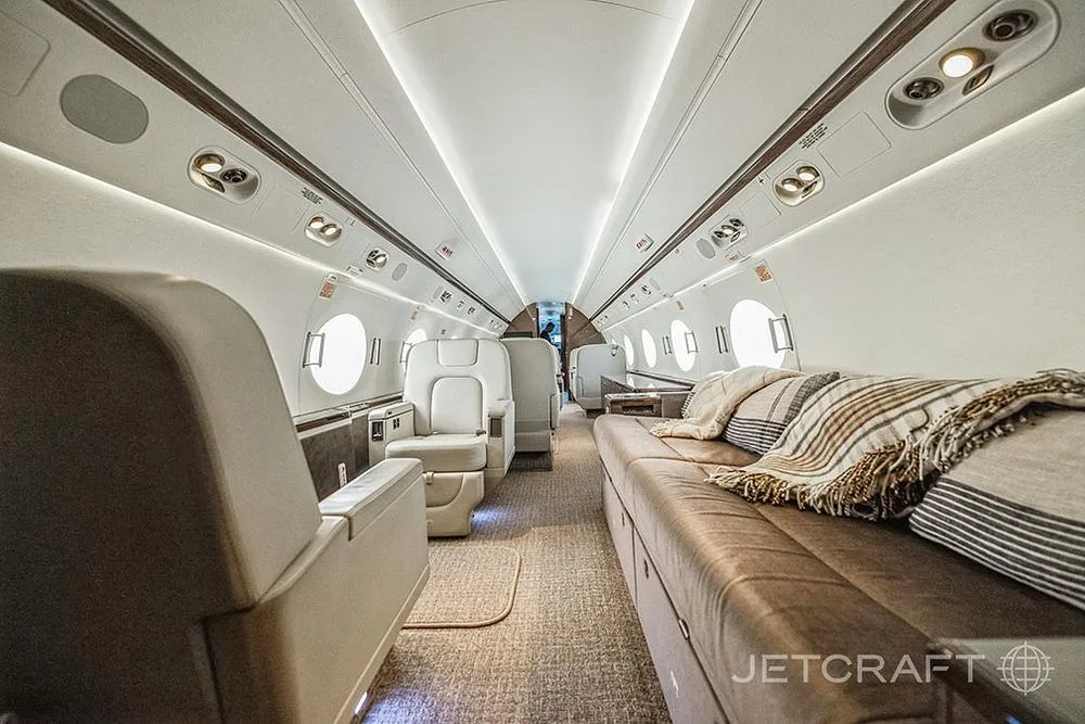 A long view of the Gulfstream G650 cabin interior highlighting a comfortable brown leather divan with throw pillows.