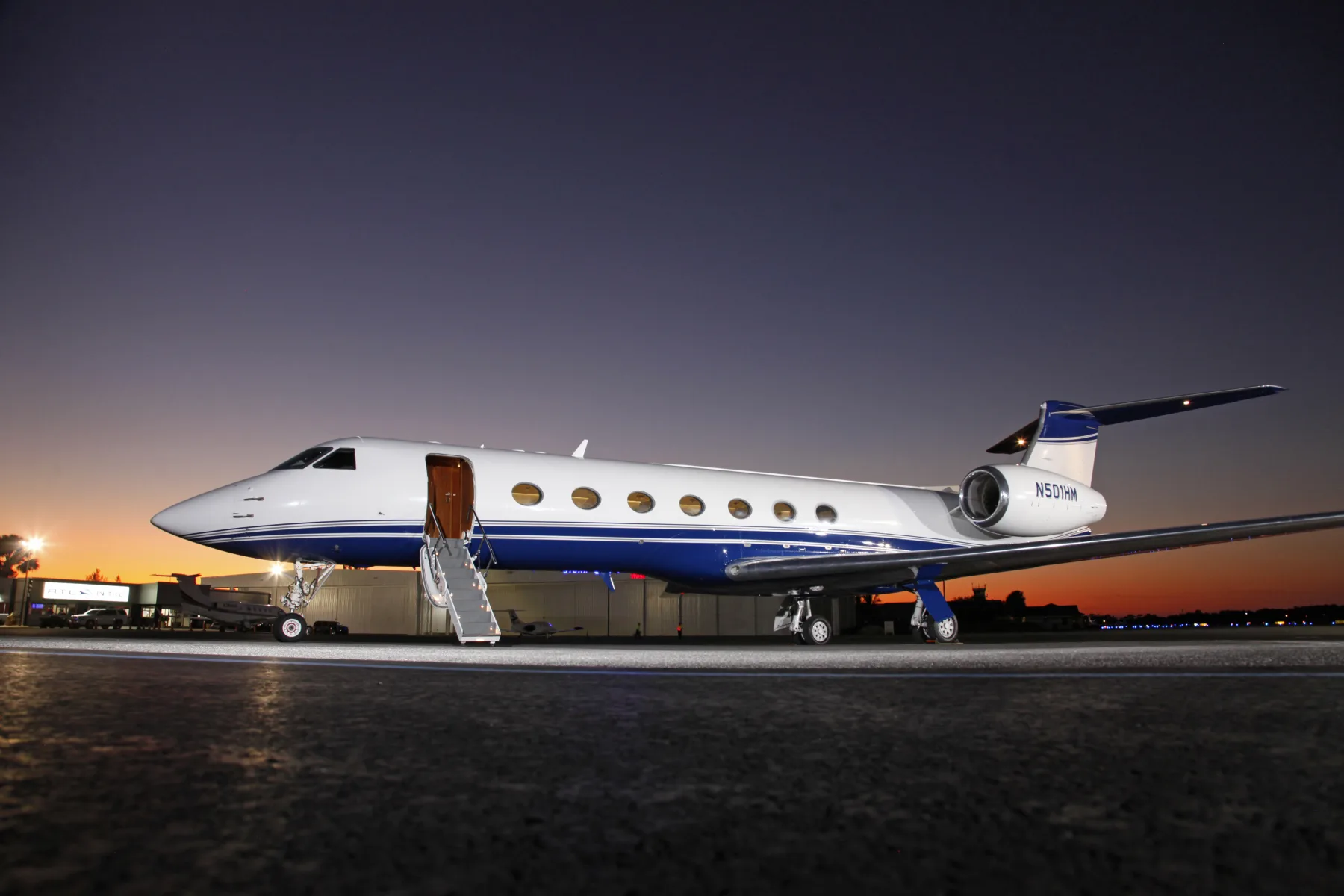 A Gulfstream jet with blue and white paint scheme is parked on the tarmac at dusk.